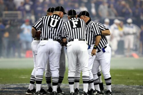 Group of sports officials in striped uniforms discussing on a football field.